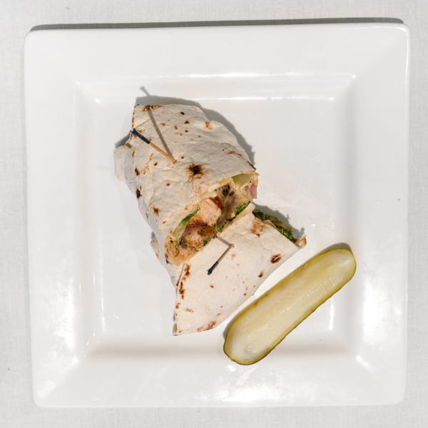 Chicken wrap cut in half with toothpicks, served with a pickle spear on a white plate.