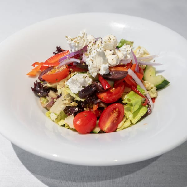 A vibrant salad with lettuce, cherry tomatoes, red onions, bell peppers, olives, and feta cheese.
