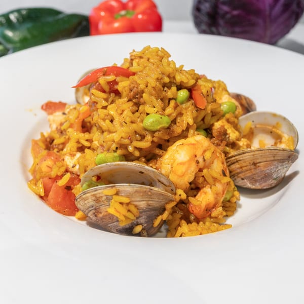 Close-up of a seafood paella dish with shrimp, clams, rice, and vegetables.