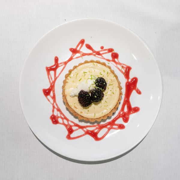 Key lime tart with whipped cream, blackberries, lime zest, and raspberry drizzle on a white plate.