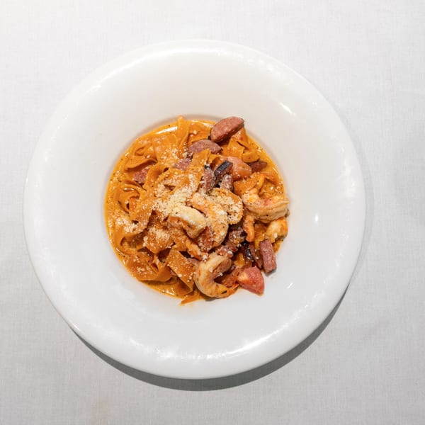 Pasta with shrimp, sausage, and parmesan cheese in a creamy red sauce, served in a white bowl.