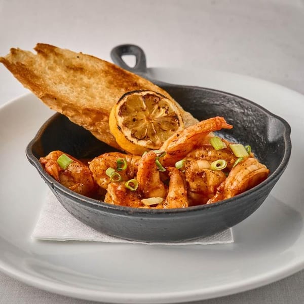 Sizzling shrimp in a black skillet with toasted bread, grilled lemon, and green onions.
