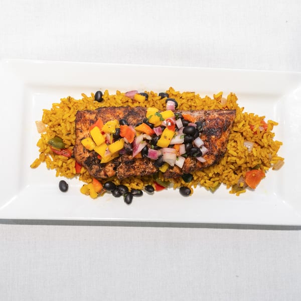 Grilled salmon with mango salsa, black beans, and yellow rice on a white rectangular plate.