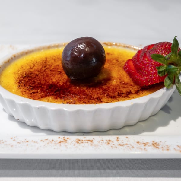 Crème brûlée in a white ramekin, topped with a chocolate truffle and a sliced strawberry.