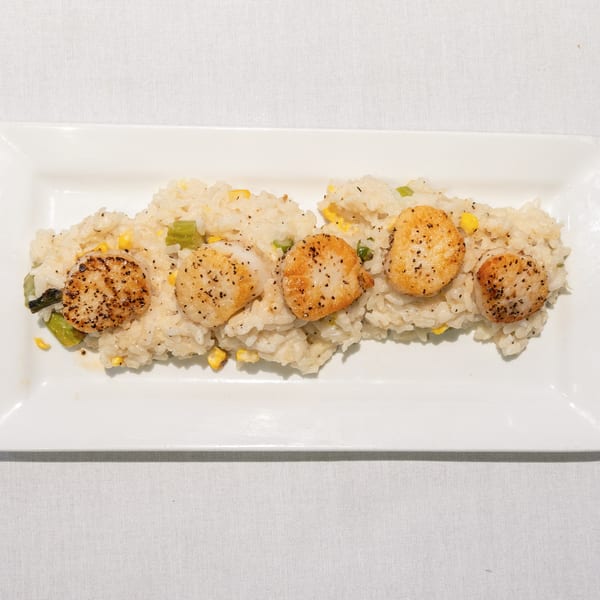 Seared scallops with black pepper on a bed of risotto with corn and asparagus on a white plate.