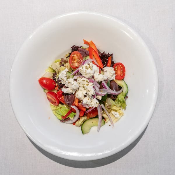 A vibrant Greek salad with feta, olives, tomatoes, cucumbers, and red onion in a white bowl.
