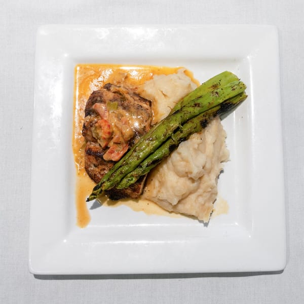 Grilled steak topped with sauce and shrimp, served with mashed potatoes and asparagus on a white plate.