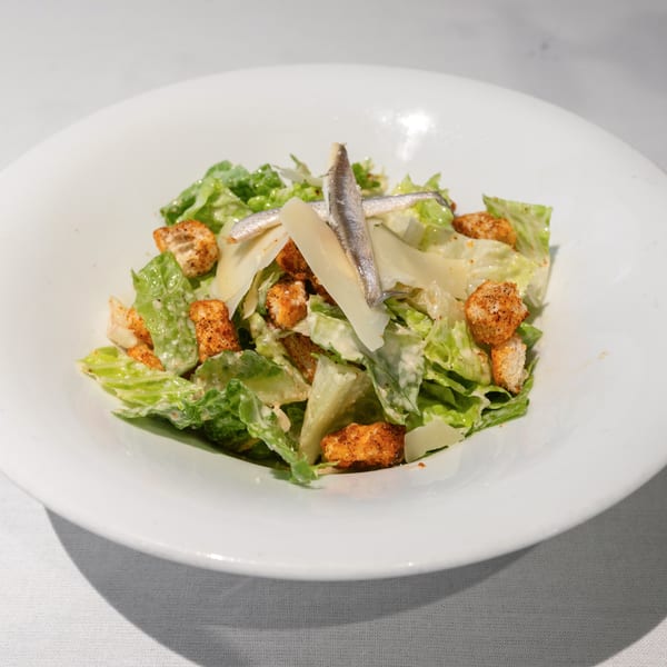 Caesar salad with romaine lettuce, croutons, parmesan cheese, and anchovies in a white bowl.